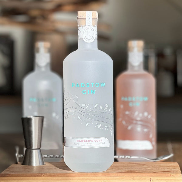 A bottle of Hawkers Cove Rose & Pink Peppercorn Gin on a wooden gin board with other bottles of Padstow Gin in the background